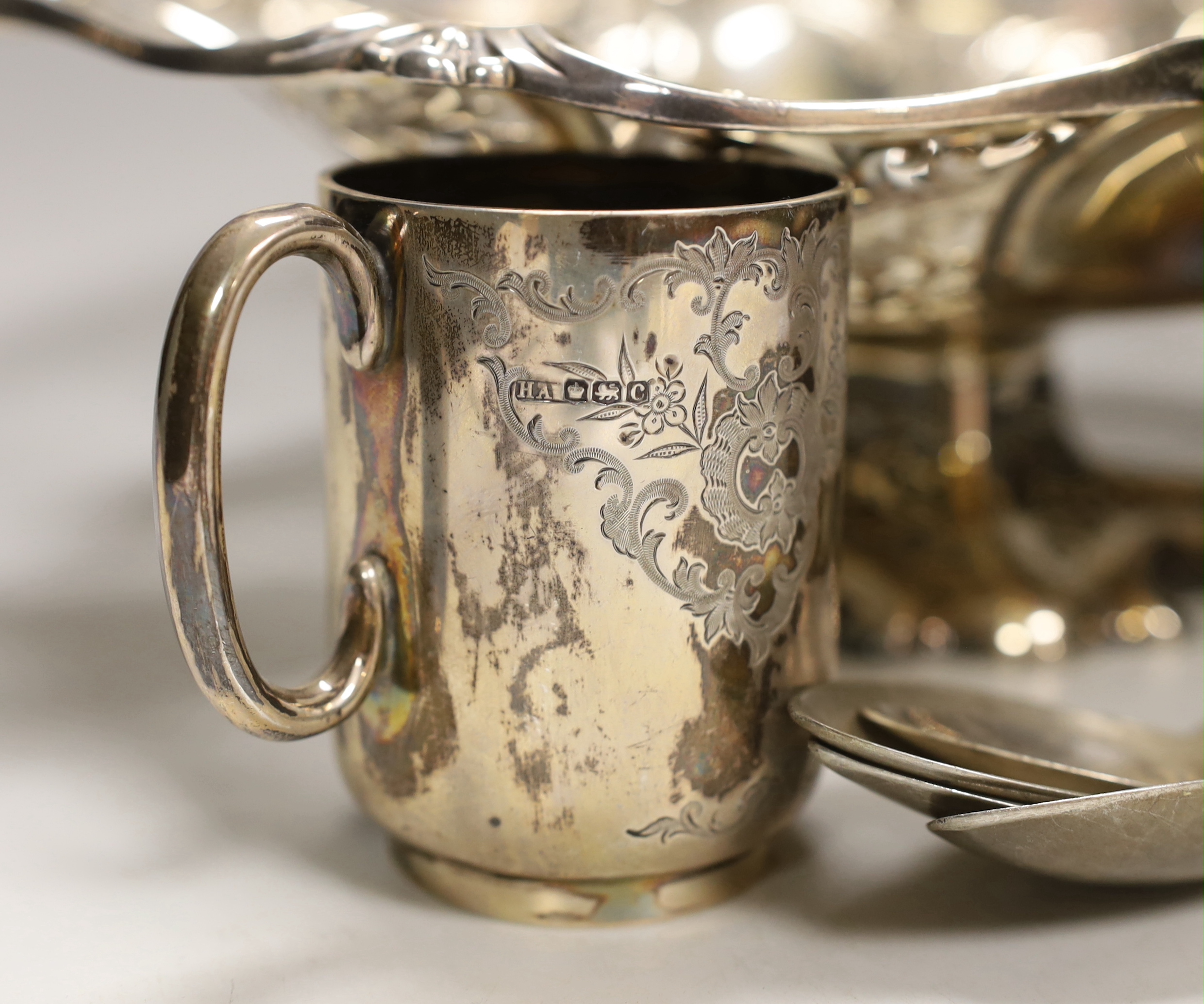 A George V silver christening mug, two silver spoons, four white metal spoons, a pierced white metal sphere? decorated with elephants and a plated bread basket.